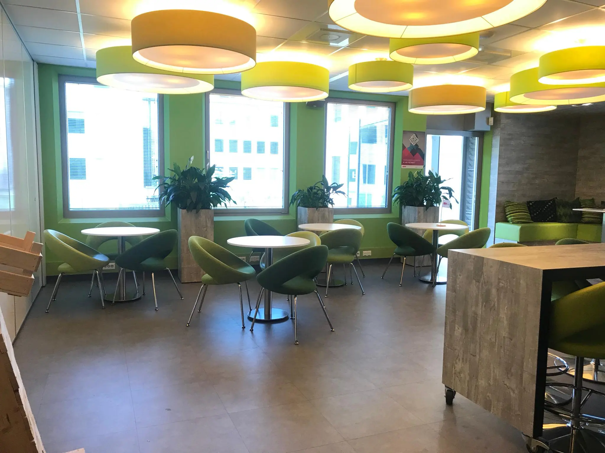 Moderne kantineruimte in Rivium Quadrant met ronde tafels, groene stoelen en grote plafondlampen.